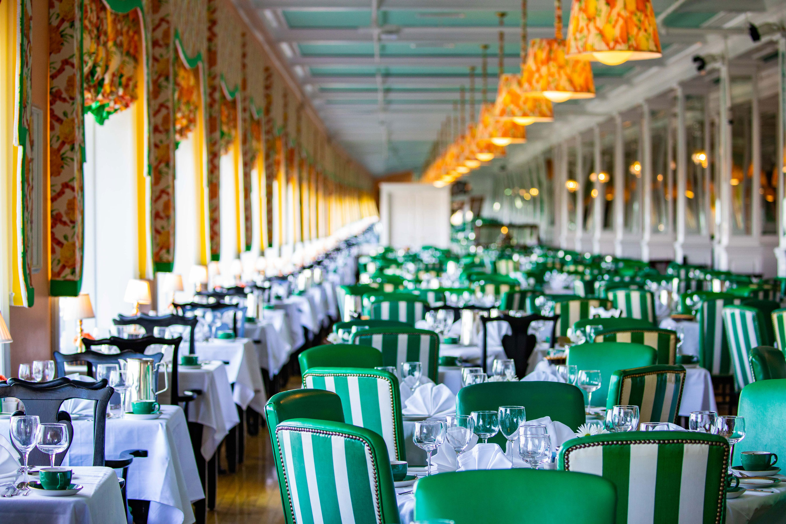 Image of The Main Dining Room with striped green and white chairs and mirrored pillars. Grand Hotel, a member of Historic Hotels since 2001, dates to 1886. It is located in Mackinac Island, Michigan.
