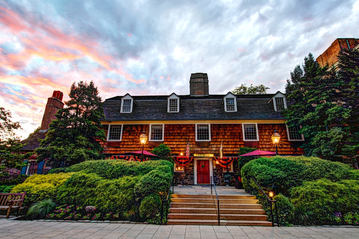 Image of the facade of The Nassau Inn (1756), a member of Historic Hotels of America since 2024. Pictured is a large building with foliage and warm lighting.