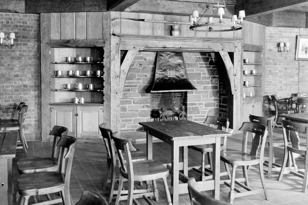 Historic image of the tap room at The Nassau Inn (1756), a member of Historic Hotels of America since 2024. Pictured are several tables and chairs around a large fireplace.