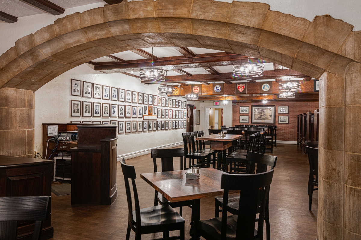 Image of the dining room at The Nassau Inn (1756), a member of Historic Hotels of America since 2024. Pictured are several tables and framed photos under an arch.