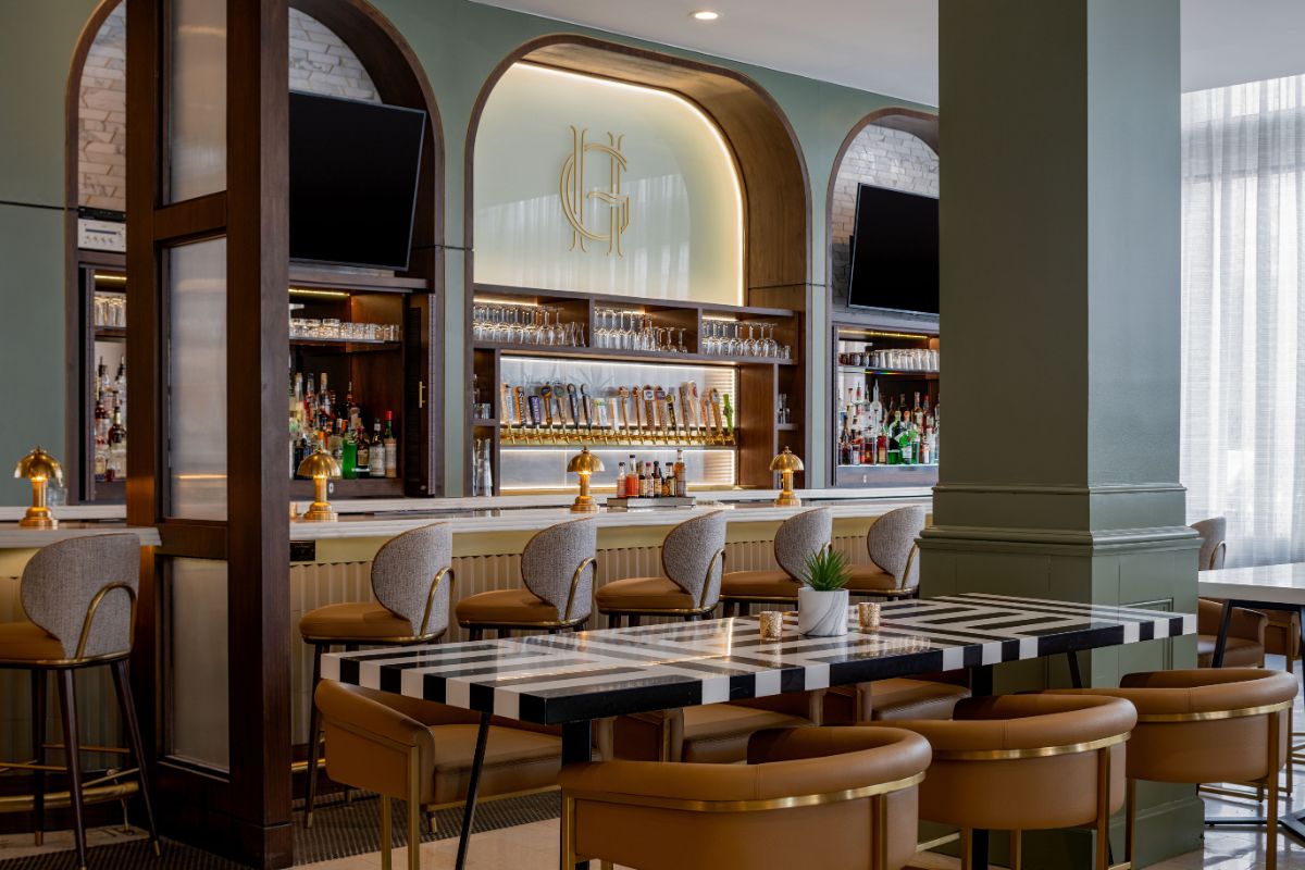 Image of a bar at Hilton Richmond Downtown (1885), a member of Historic Hotels of America since 2024. Pictured is a bar with stools and bottles behind it.